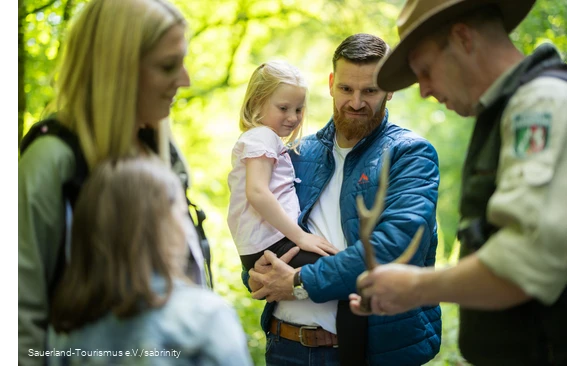 Eine Familie mit zwei Mädchen schaut interessiert auf eine Erklärung eines Rangers