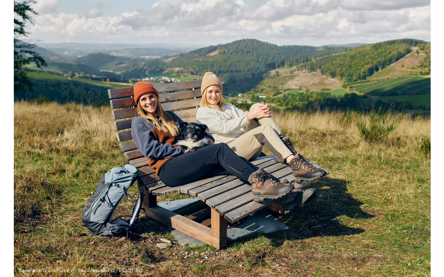 Zwei Frauen und ein Hund machen eine Pause auf einer Bank mit weiter Aussicht