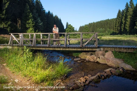 Ein Ranger steht auf einer Brücke im Schwarzbachtal