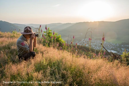 Ein Ranger sitzt am Rothaarkamm im Gras und fotografiert