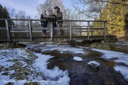 Zwei Wanderinnen mit einem Ranger auf einer Brücke im Schwazbachtal an einem kalten Wintermorgen