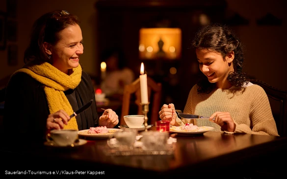 Eine Mutter mit ihrer Tochter sitzen bei gemütlichem Kerzenlicht an der Kaffeetafel mit Waffeln