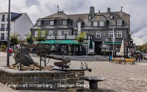 Ein Brunnen mit einem Wasserlauf mit einem Marktplatz und einem verschieferten Gebäude im Hintergrund.