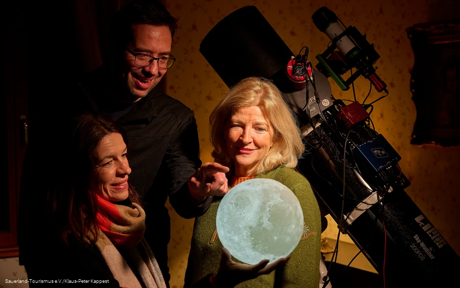 Drei Menschen schauen auf ein leuchtenes Mondmodell als Vorbereitung zum Sternegecken