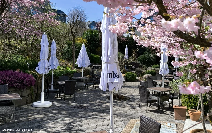 Eine Terrasse mit Sitzmöglichkeiten und Sonnenschirmen umgeben von blühenden Kirschbäumen.